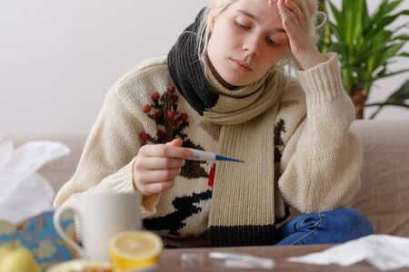 The girl in the sweater is sick sitting on the couch. Colds and flu. The patient caught a cold,...