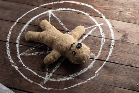 Voodoo doll on a wooden background with dramatic lighting. The concept of witchcraft and black art...