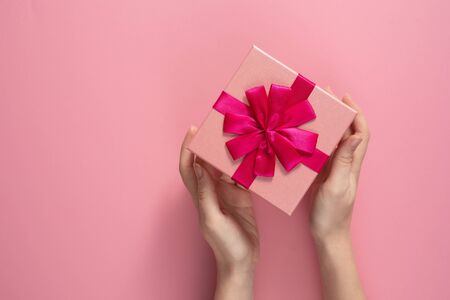 Valentine's Day celebration concept. A nice gift from a loved one. Box with a bow in female hands on a delicate pink background. Copy space.の写真素材