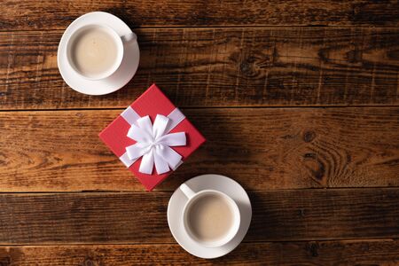 Valentine's Day celebration concept. A nice gift for your loved one. Hands of man and woman with coffee mugs on a wooden table background. Copy space. Flat lay.の写真素材