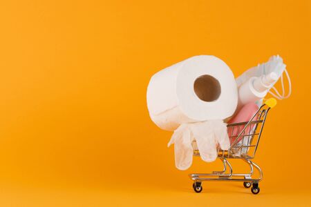 Medical mask and disinfection gloves in a shopping trolley on a yellow background. Virus protection concept. Prevention of the spread of the virus and the pandemic COVID-19.の写真素材