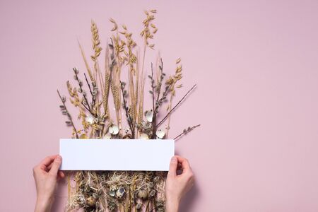 Female hands collect easter composition on a pale pink background. Dried flowers and eggs for a beautiful greeting card. The concept of Easter decorative cards.の写真素材