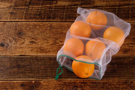 Zero waste, plastic free recycled textile produce bag for carrying fruit orange or vegetables, a wooden surface. Reusable using. Copy space.の写真素材