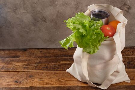 Eco-friendly groceries bag. Reusable shopping bag with fresh fruits and greens on wooden background....