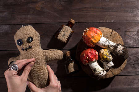 Voodoo doll on a wooden background with dramatic lighting. A sacking doll on a wooden background and bottles with a poisonous substance and amanita mushrooms. Pierce with a club.の写真素材