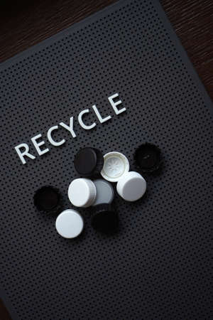 Black and white lids on a grey board with recycle wordの写真素材