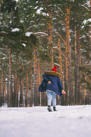 Girl has back pain after falling on wet snow. Funny posture. Walking away. Be careful on a wet melting snowの写真素材