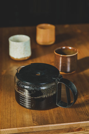 Coffepot with three cups on a wooden table in dark studio