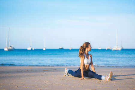 Athletic girl warming up on the beach. Beach yoga. Stretching. Healthy lifestyleの写真素材