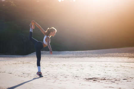 Athletic girl warming up on the beach. Beach yoga. Stretching. Healthy lifestyle
