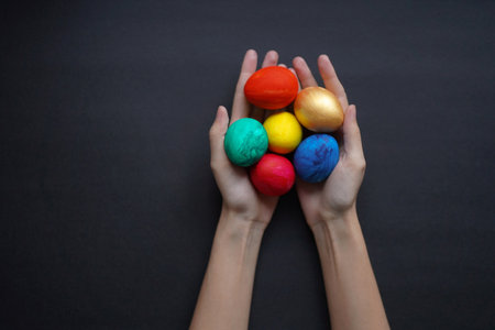 Six colored easter eggs in thin hands on a black background. Minimalist, copy spaceの写真素材