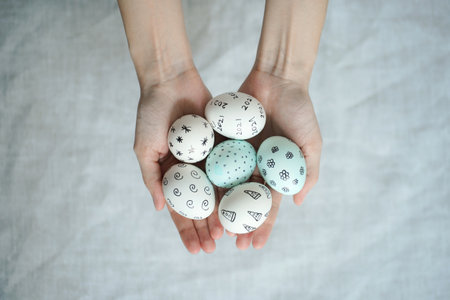 Easter eggs with hand-drawn patterns in thin hands above linen cloth background. Easter concept