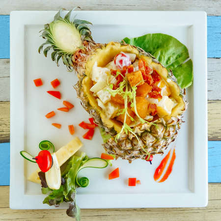 Fancy salad with chopped fried bacon, vegetables and pineapple cubes in a pineapple cut in half. Top viewの写真素材