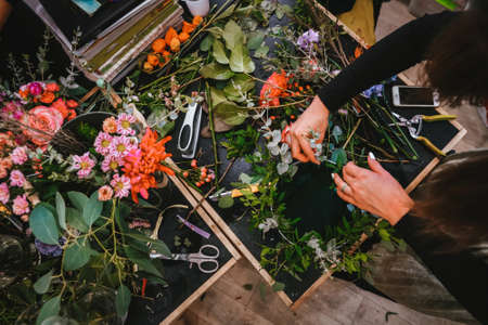Watching the florist work from above. Assembling a wreath of flowers, leaves and thin branches. Stylish floral arrangementsの写真素材