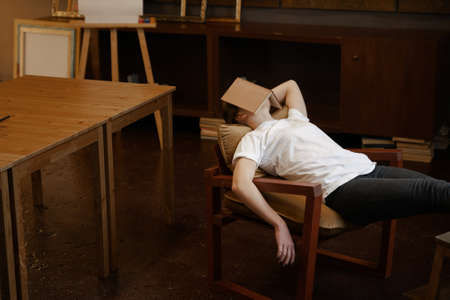 Girl in white t-shirt sleeps in dark cozy art class with book on face. Boring school lessonの写真素材