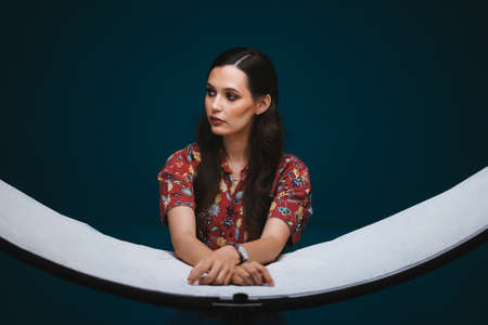Caucasian girl with makeup and styling leans on reflector in the studio on dark wall background....