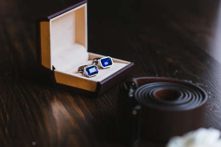 Mens cufflinks with a blue stones and a belt on a dark wooden table. Gift idea for a manの写真素材