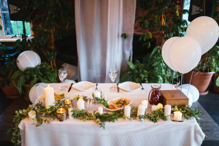 Wedding table of the bride and groom with white balloons and candles and decorations made of green...