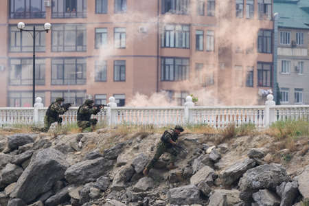 Kaspiysk, Dagestan, Russia - July 25, 2021: Three soldiers in military uniforms are fighting at residential buildings during military exercises. Smoke from bullets and grenades.のeditorial素材