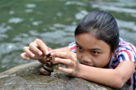 Ciamis, Indonesia - 31 October 2020: A girl is stacking stones in a river, Ciamis, West Java, Indonesiaのeditorial素材