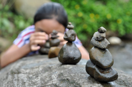 Ciamis, Indonesia - 31 October 2020: A girl is stacking stones in a river, Ciamis, West Java, Indonesiaのeditorial素材