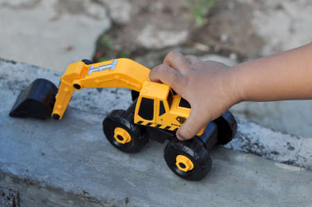 Children holding yellow excavator vehicle toy outdoor