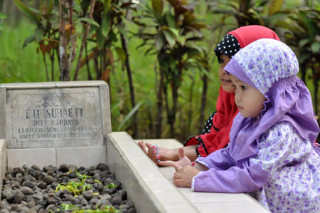Ciamis, Indonesia - July 17, 2015 : Two little girls praying beside their grandmother's grave in Ciamis, West Java - Indonesiaのeditorial素材