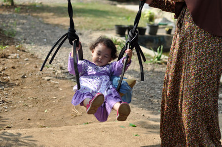 West Java, Indonesia - July 17, 2015 : A little girl is playing on a swing with her mother in a village in West Java, Indonesiaのeditorial素材