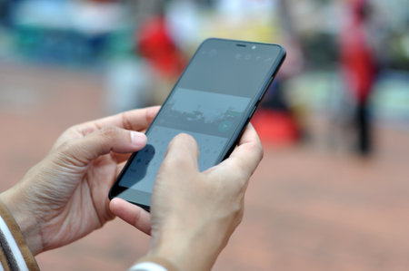 Close-up of a young woman's hand using a mobile phone in a city parkの写真素材