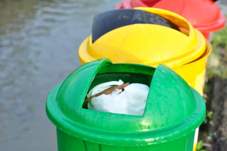 Three green, yellow and red trash cans by the riverの写真素材