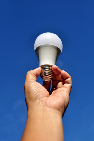 Holding light bulb LED blue sky background selective focus