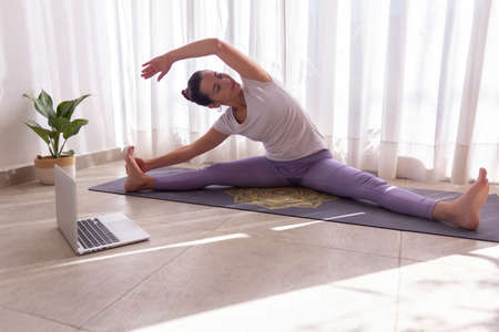 overhead shot of woman practicing yoga online with a computer in a bright room