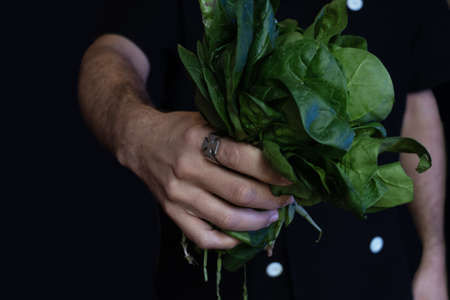 close-up of man with maltese cross ring holding a bouquet of spinach