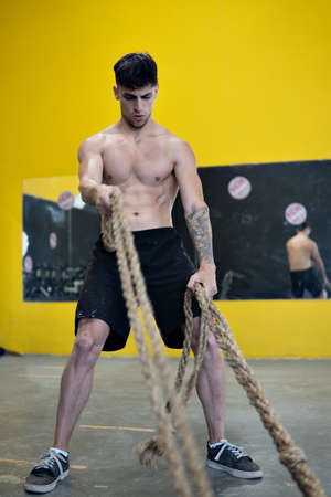 Fit man working out with battle ropes at fitness gym