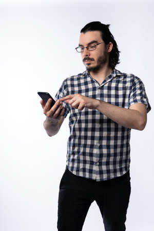 Portrait of young man with glasses using smartphone on white background.の写真素材