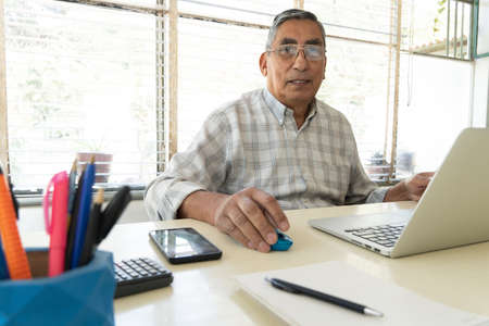 Mature man looking at camera sitting in front of laptop computer.の写真素材