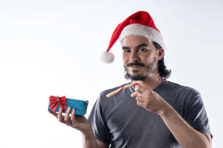 Medium shot portrait of smiling Latino man with red Santa Claus hat looking at camera holding Christmas presents , isolated on white background. Positive emotions, facial expressionsの写真素材