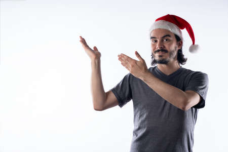 Young Latino man in Santa Claus hat, with a smile showing his hands to the side. White backgroundの写真素材