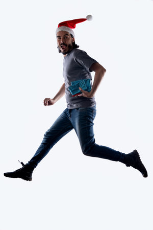 Latino man in Santa Claus hat jumping with Christmas giftsの写真素材