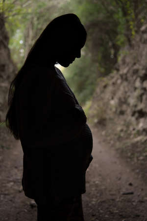 Full shot of silhouette of pregnant woman outdoors in the middle of the road. Backlit figure, nature background. Selective focus.の写真素材