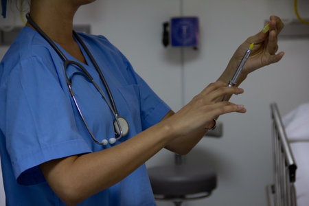 Doctor holding a syringe in a hospital room. Portrait without face with stethoscope and light blue uniform.の写真素材