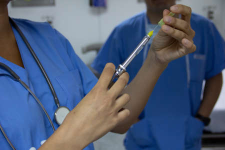 Doctor holding a syringe in a hospital room in the background another doctor observing. Selective...