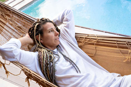 Blonde woman with dreadlocks relaxing with her eyes closed in a woven hammock.