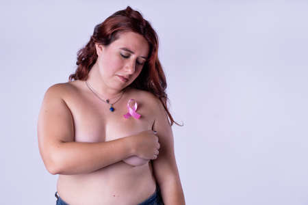 Afro woman covering her breast holding pink ribbon on white background. Breast cancer awareness concept.の写真素材