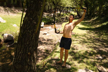 Handsome muscular man is training outdoor on TRX. Total Body Resistance Exercises.