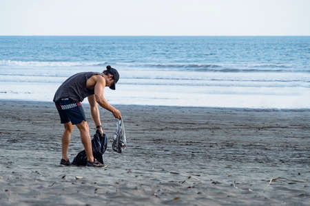 Young man picking up trash on the beach. Save the planet. CopySpace.の写真素材