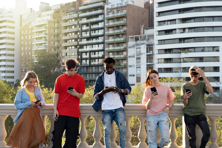 Young people looking down at cellular phone. Teenagers leaning on a wall and texting with their...