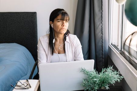 Latina woman working in her apartment looks towards window. Home office concept, overwork, deadlines...