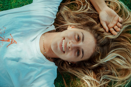 Portrait of beautiful young woman looking at camera and smiling lying on grass.の写真素材