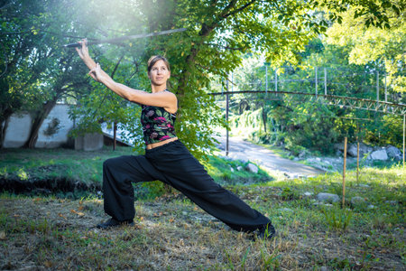 A serene and focused woman is practicing the ancient Chinese martial art of tai chi with her sword by the tranquil river.の写真素材